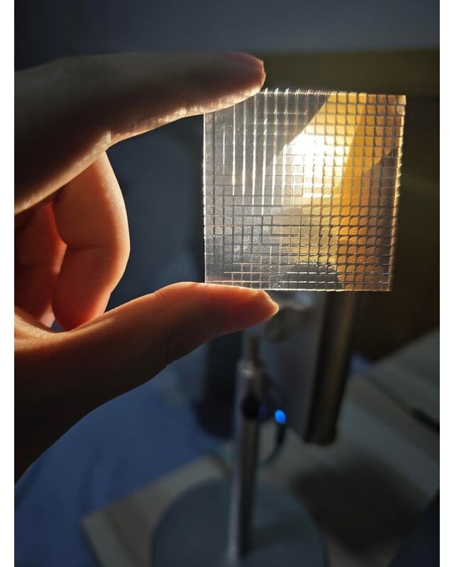 The lens held between two fingers in front of a lamp, showing its grid of square facets